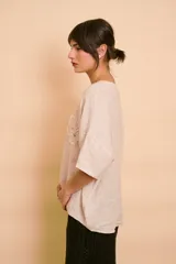 Blusa holgada color beige con mangas cortas y cuello redondo. Presenta apliques bordados con detalles de perlas y lentejuelas en el frente.