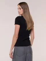 Remera básica de corte al cuerpo con textura acanalada, cuello redondo y mangas cortas. Presenta una pequeña placa metálica decorativa en el borde inferior.