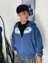 Campera con cierre frontal y capucha, color azul, con estampado gráfico ovalado en el pecho.