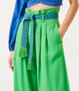 Pantalón de lino verde, modelo palazzo, con cintura alta, pliegues frontales y un cinturón bordado en tonos de verde y azul.
