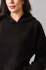 Buzo tipo canguro color negro, con capucha, mangas largas y corte holgado. Presenta un diseño minimalista sin estampados.