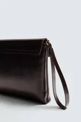 Bolso de mano tipo sobre color marrón oscuro, confeccionado en cuero. Cuenta con cierre de solapa con broche metálico dorado y asa de mano.