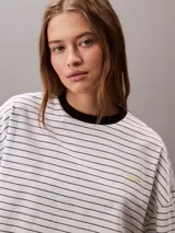 Remera Calvin Klein de corte boxy y largo cropped, con diseño de rayas horizontales, cuello redondo en contraste y mangas cortas con hombros caídos. Presenta un pequeño logo bordado en el pecho.