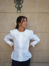 Camisa de lino blanca con cuello redondo amplio, apliques de encaje y broderie en el cuello, la botonera y los puños anchos, de manga larga abuchonada.