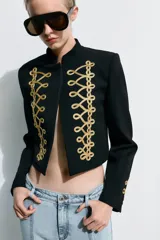 Blazer crop color negro, con cuello subido, manga larga y cierre frontal con botones ocultos. Presenta detalles de alamares bordados a contraste en color dorado en el frente y en los puños.