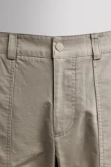 Pantalón de corte tapered fit color beige, confeccionado en tejido ligero de algodón con estructura rip stop. Cuenta con bolsillos de plastrón delanteros con acceso curvado, pinzas en las rodillas para mayor movilidad, y cierre frontal con cremallera y botón a presión.