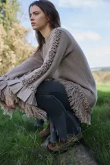 Sweater de lana merino color beige, con silueta amplia y relajada. Presenta mangas largas con volumen, terminaciones con volados de lino y flecos en los puños y en el ruedo, además de detalles trenzados a lo largo de las mangas.