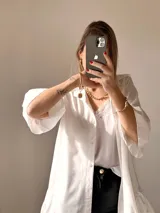 Camisa blanca de tejido suave tipo seda, con mangas tres cuartos y volados irregulares en mangas y ruedo. Tiene un largo ligeramente mayor en la espalda.
