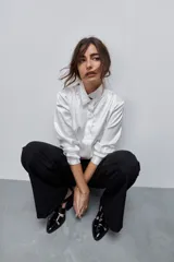 Camisa blanca de calce relajado con acabado satinado y brillo sutil, cuello clásico, cierre frontal con botones y mangas largas con puños.