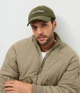 Gorra de béisbol con visera curva, confeccionada en tejido de pana (cotelé) color verde oliva. Presenta un bordado frontal con la inscripción 'Future Studios' en color blanco y cuenta con un sistema de ajuste mediante hebilla metálica en la parte posterior.