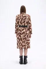 Vestido tipo camisa de corte holgado, con cuello clásico, cierre frontal de botones y mangas largas. Presenta un estampado de hojas en tonos marrones y beige.