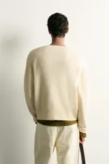 Cárdigam relaxed fit de punto tejido en color beige claro, con cuello en V, manga larga, acabados en rib y cierre frontal de botonadura con botones en tono carey.