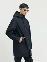 Gabardina con capucha de corte recto y largo medio. Cuenta con cierre frontal engomado, cartera con botones a presión, bolsillos laterales y tejido repelente al agua y al viento.
