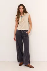 Jean tostado de corte wide leg, tiro medio con presillas y lazo ajustable en la cintura. Presenta bolsillos delanteros y traseros, costuras decorativas verticales y terminación desmechada en el ruedo.
