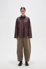 Sobrecamisa de cuero sintético en tono bordó oscuro, con cuello clásico, cierre frontal oculto y un bolsillo aplicado en el pecho. Presenta un corte holgado con mangas largas y puños rectos.