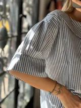 Blusa celeste y blanca a rayas verticales, con corte boxy, mangas cortas amplias y cuello Peter Pan.