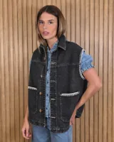 Chaleco de jean negro 100% algodón, con cuello camisero, cierre frontal con botones y bolsillos delanteros con costuras decorativas blancas acontraluz.