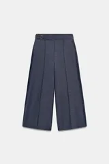 Pantalón culotte de tiro medio con pernera ancha y corta. Presenta nervios marcados en la parte delantera, bolsillos laterales y cierre frontal con cremallera, botón interior y hebilla ajustable en la cintura.