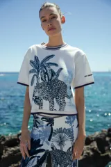 Top de tejido de algodón blanco con cuello redondo y mangas cortas. Presenta estampado de palmeras y un leopardo en tonos azules.