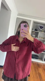 Camisa de corte oversize con estampado de rayas verticales finas, cuello clásico, cierre frontal con botones y bolsillo en el pecho.