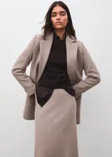 Abrigo de paño color beige, con diseño cruzado de doble botonadura, solapas clásicas y bolsillos laterales con solapa. Presenta un corte estructurado y elegante.