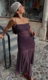 Conjunto de dos piezas compuesto por un top de tirantes finos con escote recto y fruncido, y una falda midi de corte sirena con bajo asimétrico. Ambas prendas presentan un estampado de lunares blancos sobre fondo violeta oscuro.