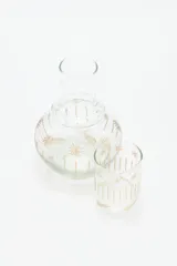 Jarra de vidrio transparente con diseño de estrellas doradas. Incluye un vaso de vidrio transparente con diseño de líneas verticales doradas.