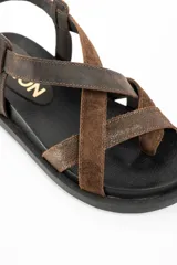 Sandalias de cuero marrón con tiras cruzadas en el empeine, suela chunky negra y hebilla metálica de ajuste en el talón.