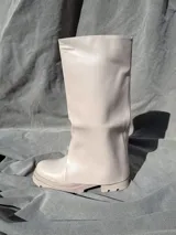 Bota de caña alta color blanco de cuero sintético con suela track y abertura lateral.