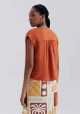 Blusa naranja sin mangas con escote en V y detalle de frunces en los hombros.