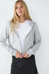 Campera con capucha y cierre frontal de cremallera, confeccionada en tejido gris melange con bolsillos estilo canguro y puños y bajo de canalé.
