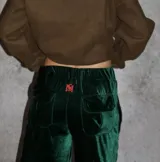 Pantalón cargo de terciopelo verde oscuro, de corte holgado, cintura elástica y bolsillos con solapa en la parte trasera. Cuenta con detalle de bordado rojo en la parte superior.