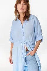 Vestido camisero largo de lino italiano color celeste, de corte relajado, con mangas caídas, jareta ajustable en la cintura, cierre frontal de botones y bajo con volado fruncido.