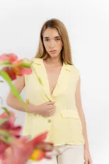 Chaleco sastrero de lino color amarillo pastel, con cuello solapa, cierre frontal con botones y bolsillos decorativos con solapa en la parte inferior.