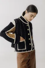 Chaqueta de punto con diseño color block en negro, beige y marrón. Presenta cuello redondo, cierre frontal con botones grandes, bolsillos frontales y detalles de costuras decorativas verticales en color claro.