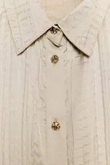 Camisa de manga larga con cuello solapa, confeccionada en tejido satinado con textura efecto arrugado y cierre frontal con botones dorados.