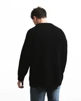 Sweater negro de punto con cuello redondo y corte holgado. Diseño con motivo de zurcido en la manga izquierda.
