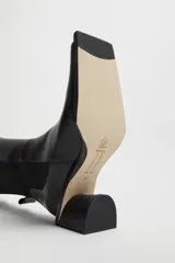 Botas negras de cuero brillante a media pantorrilla con taco de cuero en cascada de 5cm y punta cuadrada alargada. Panel elástico en el lateral trasero de la pantorrilla y lengüeta.