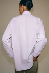 Camisa de manga larga confeccionada en hilatura con mezcla de algodón, con cuello solapa, bajo redondeado y cierre frontal oculto con botones.