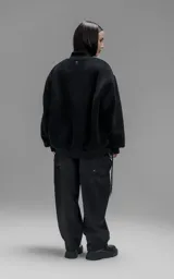 Campera estilo bomber unisex, confeccionada en una combinación de corderito sintético y paneles de ripstop. Presenta un diseño utilitario con múltiples bolsillos frontales con cierres y broches a presión, cuello, puños y ruedo en ribb elástico.