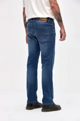 Jean de corte slim, color azul medio, con diseño clásico de cinco bolsillos, cierre frontal con botón y cremallera.