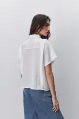 Camisa negra de manga corta, con cuello mao y cierre frontal de botones, de silueta amplia y tejido liviano con textura sutil.