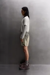 Pantalón corto de trail running color beige, confeccionado en tejidos técnicos ligeros y elásticos. Cuenta con forro interior, cintura elástica ajustable con cordón, bolsillos traseros laterales multifunción, bolsillo trasero central con cremallera, bajo con costura termofijada y aberturas laterales. Incluye logo estampado en la pernera.