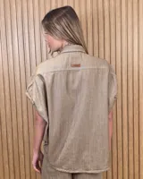 Camisa de manga corta color beige, de corte holgado, con cuello camisero y cierre frontal de botones.