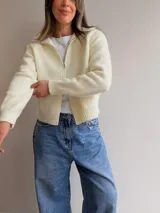 Cardigan tejido de textura suave con cierre frontal de doble vía, cuello alto y mangas largas. Presenta terminaciones en rib en puños y cintura, con un diseño versátil y moderno.