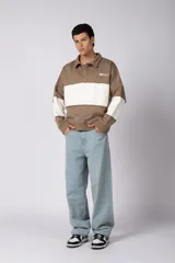 Buzo tipo polo de calce relajado con diseño de bloques de color en tonos marrón y blanco. Presenta cuello polo, cierre frontal parcial y logo estampado en el pecho. Confeccionado en tejido pesado con estructura.