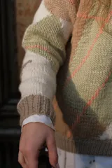 Cárdigan de punto tejido a mano con diseño de rombos en tonos neutros, beige y verde suave. Presenta escote redondo, cierre frontal con botones y mangas largas con diseño holgado.