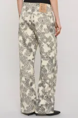 Pantalón de tiro medio y calce holgado, confeccionado en 100% algodón de peso medio con un estampado exclusivo de diseño ornamental en tonos blanco y gris oscuro. Cuenta con una cartera asimétrica cruzada en la cintura, bolsillos y sutiles desgastes manuales con pequeñas roturas localizadas.
