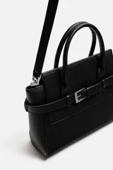 Bolso bandolera negro con detalle de cinturón, compartimento principal con cierre de imán, bolsillo interno con cremallera, doble asa de mano y asa de hombro ajustable y extraíble.