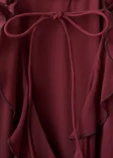 Vestido largo bordó con volantes en el cuello y mangas largas con volantes en los puños, diseño oversize y cierre de lazo delantero.